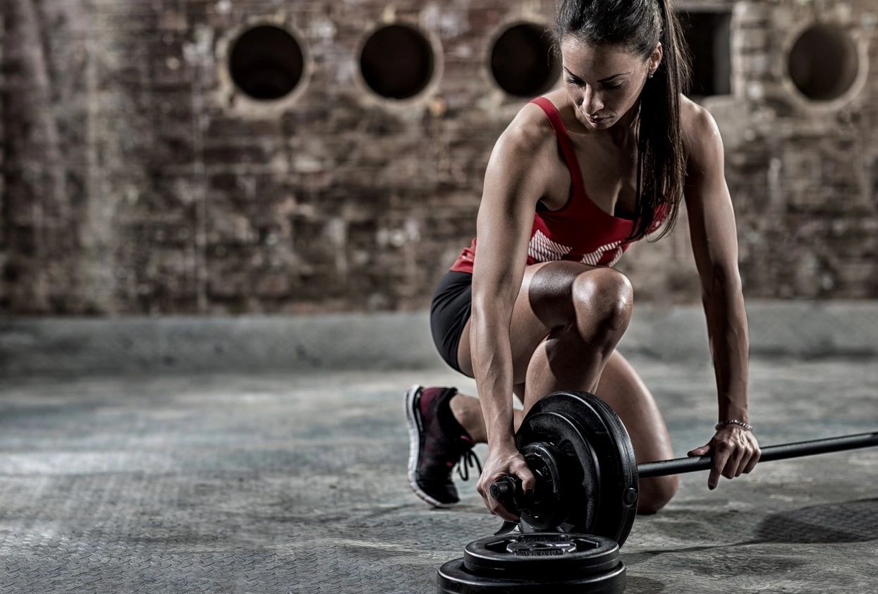 A woman is squatting down with a barbell.