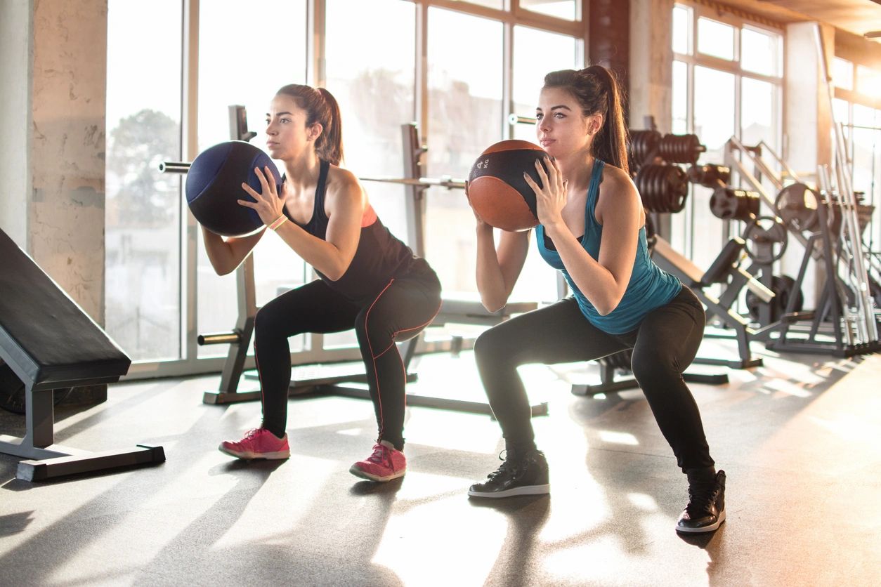 Two women are doing squats in a gym.