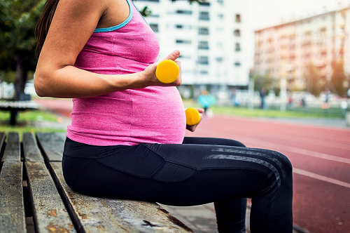 A pregnant woman holding two oranges on top of a bench.
